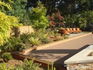 Eine große Terrasse, umgeben von Gräsern und Bäumen, mit Ideen für niedrige Terrassenmöbel aus Holz mit orangefarbenen Kissen.