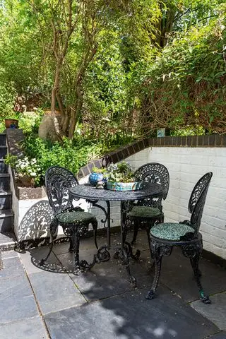 Schmiedeeiserner Tisch und Stühle in einer kleinen, mit Schiefer gepflasterten Terrasse mit weiß gestrichenen Wänden und Kletterpflanzen.