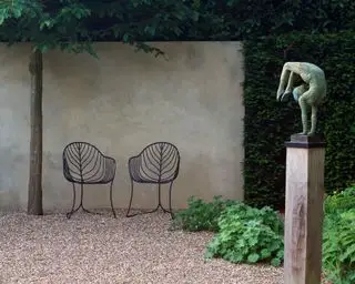 Skulptur auf einem Sockel neben einer Gartenmauer