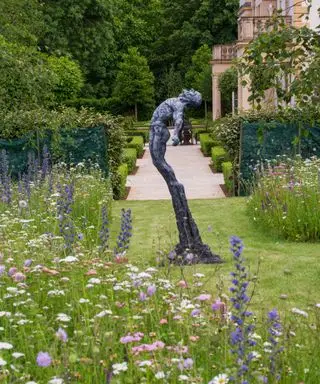 figurative Gartenskulptur aus Bronze neben einer Blumenwiese