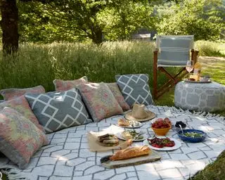Gartendeko-Ideen mit einem auf Gras ausgelegten Teppich mit Kissen und Picknick-Essen