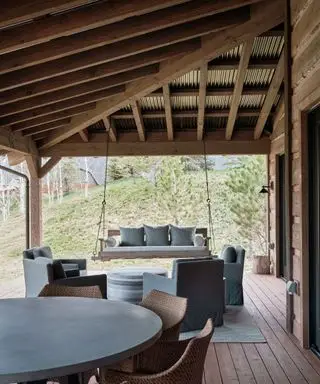 Terrazza esterna, portico con soffitto rivestito in pannelli di legno scuro e copertura in metallo, area salotto con poltrone e pouf arrotondato, zona pranzo con tavolo e sedie arrotondati, divano a dondolo sospeso al soffitto, soffitto in legno scuro