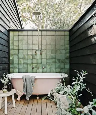 Bagno esterno con vasca rosa contro parete piastrellata verde