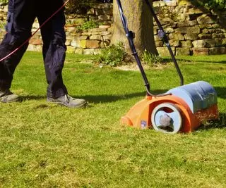 osoba używająca wertykulatora do usuwania mchu i zanieczyszczeń z trawnika