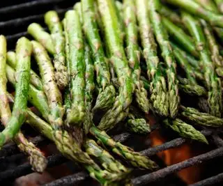Un gros plan d'asperges presque finies de cuire sur un gril à charbon de bois