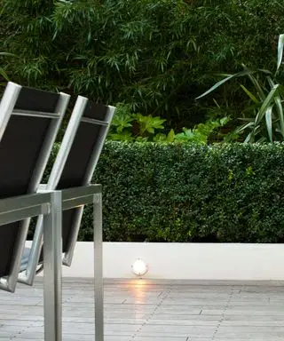 Luci solari di basso livello integrate in un muretto accanto a una siepe verde