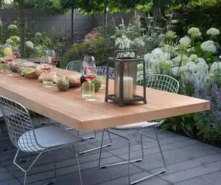 Blick auf die Terrasse mit Gartenmöbeln, schwebendem Tisch und Stühlen, Blumenrabatten mit Hortensien