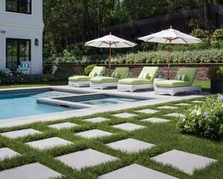 Un espace piscine avec des pavés enfoncés dans la pelouse et des chaises longues vertes et blanches sur un côté