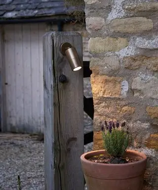 Un'inquadratura ravvicinata di un riflettore che illumina un vaso di lavanda davanti a un muro di mattoni