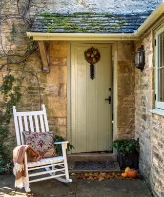 Un esempio di idee per l'illuminazione del portico anteriore che mostra una porta d'ingresso verde con una sedia a dondolo bianca e un'applique