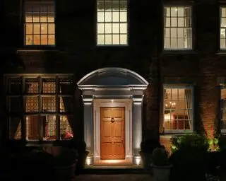 Un esempio di idee per l'illuminazione del portico anteriore che mostra un portico illuminato con una porta d'ingresso in legno e finestre a ghigliottina