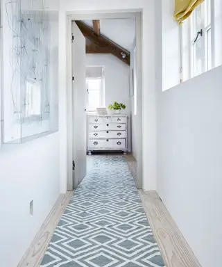 Idées de décoration de couloir avec un tapis à motifs bleu pâle et une commode en miroir au bout du couloir blanc.