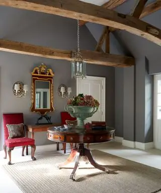 Des antiquités dans une idée de couloir classique avec des murs gris, une table ronde et un miroir doré.