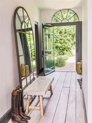 Un grand miroir adossé au mur d'un couloir, avec une banquette et du parquet.