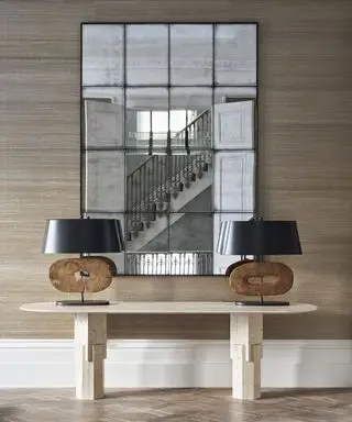 En gangtapetidé med brun gressduk og stort speil bak inngangsbord med moderne lamper