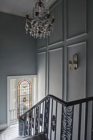 Escalier avec fuseaux ornés, vitrail palier, lustre au-dessus et applique murale