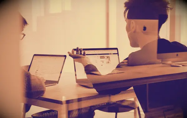 Two people discussing something while looking at their laptops.