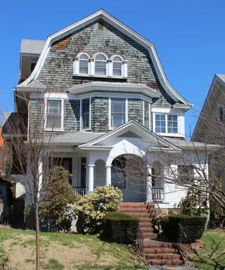 maison de style colonial gris et blanc avec toit en mansarde et marches rouges