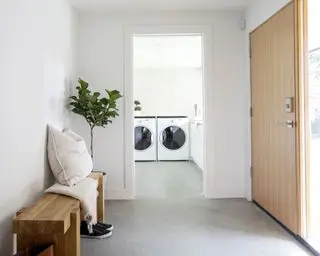 Sous-sol avec porte d'entrée et banc, et buanderie par porte avec sol gris et murs blancs