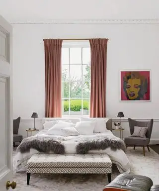 Camera da letto principale con letto matrimoniale davanti alla finestra, ottomana stampata e tappeto grigio chiaro.