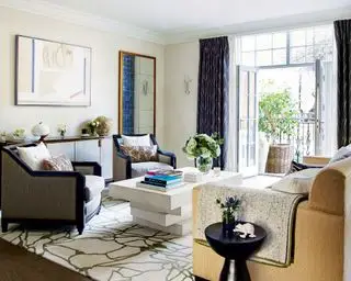 伝統的な家具、ダーク色のカーテン、模様入りの敷物を備えたベージュのリビングルームのアイデア