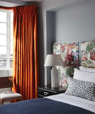 Camera da letto grigio-blu con testiera floreale e tende arancioni