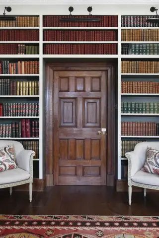 양쪽과 위쪽에 책 선반이 있는 나무 문, 나무 바닥과 러그가 있는 안락의자 2개