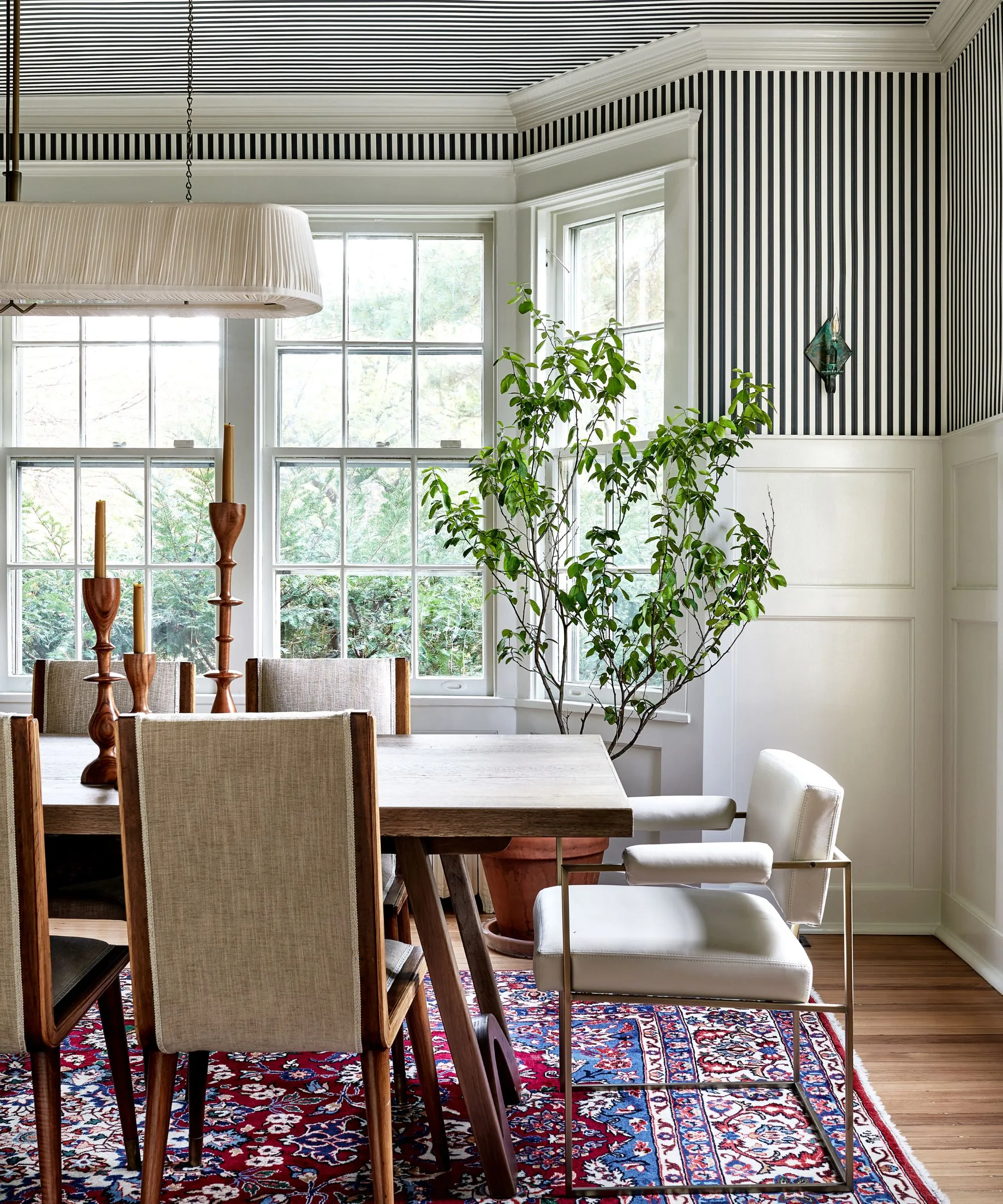 Jedáleň s pruhovanou tapetou koruna lišta veľké arkierové okná drevený jedálenský stôl moderný stôl drevené stoličky a rastlín' loading='lazy' title=