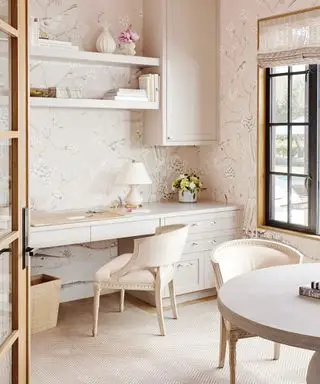farger som passer til lys rosa, hjemmekontor med lys rosa tapet, steinskap og stoler, svart vindu i crittall-stil, persienner, åpne hyller, sildebeinskremteppe