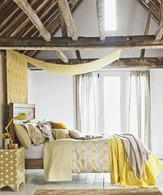 Chambre, charpente bois avec poutres en chêne, lit rustique, coussins et oreillers assortis, couette fleurie. Porte-fenêtres, marquise à losanges