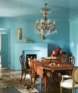 어두운 목재 가구, 샹들리에, 동물 무늬 깔개, 목재 바닥을 갖춘 청록색으로 칠해진 식당