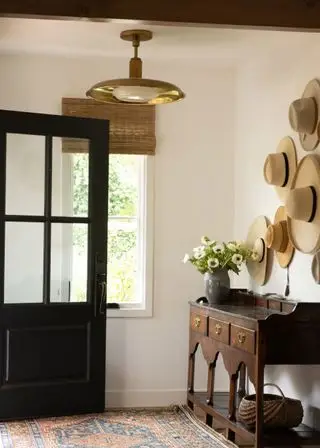 Idées de décoration de ferme, couloir peint en crème, tapis à motifs, store, console en bois, chapeaux de paille au mur, plafonnier doré