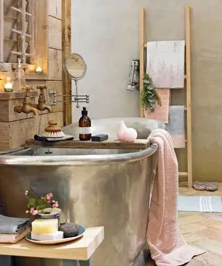 Salle de bains luxueuse de style naturel avec baignoire en étain poli, serviettes aux couleurs pastel et onguents luxueux.
