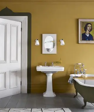 Une palette de couleurs automnales dans une salle de bain avec murs ocre jaune, lavabo blanc et baignoire grise