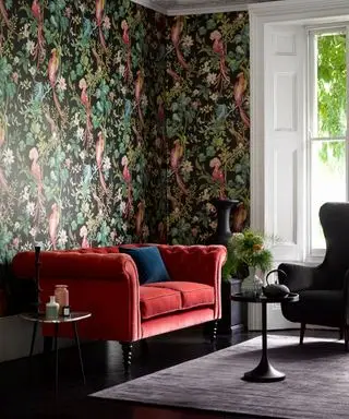 couleurs qui vont avec le rouge, salon avec sol noir, fauteuil noir, tables d'appoint et vase, papier peint avec feuilles traînantes et perroquets sur fond noir, canapé rouge, tapis gris foncé, boiseries blanches et volets d'origine