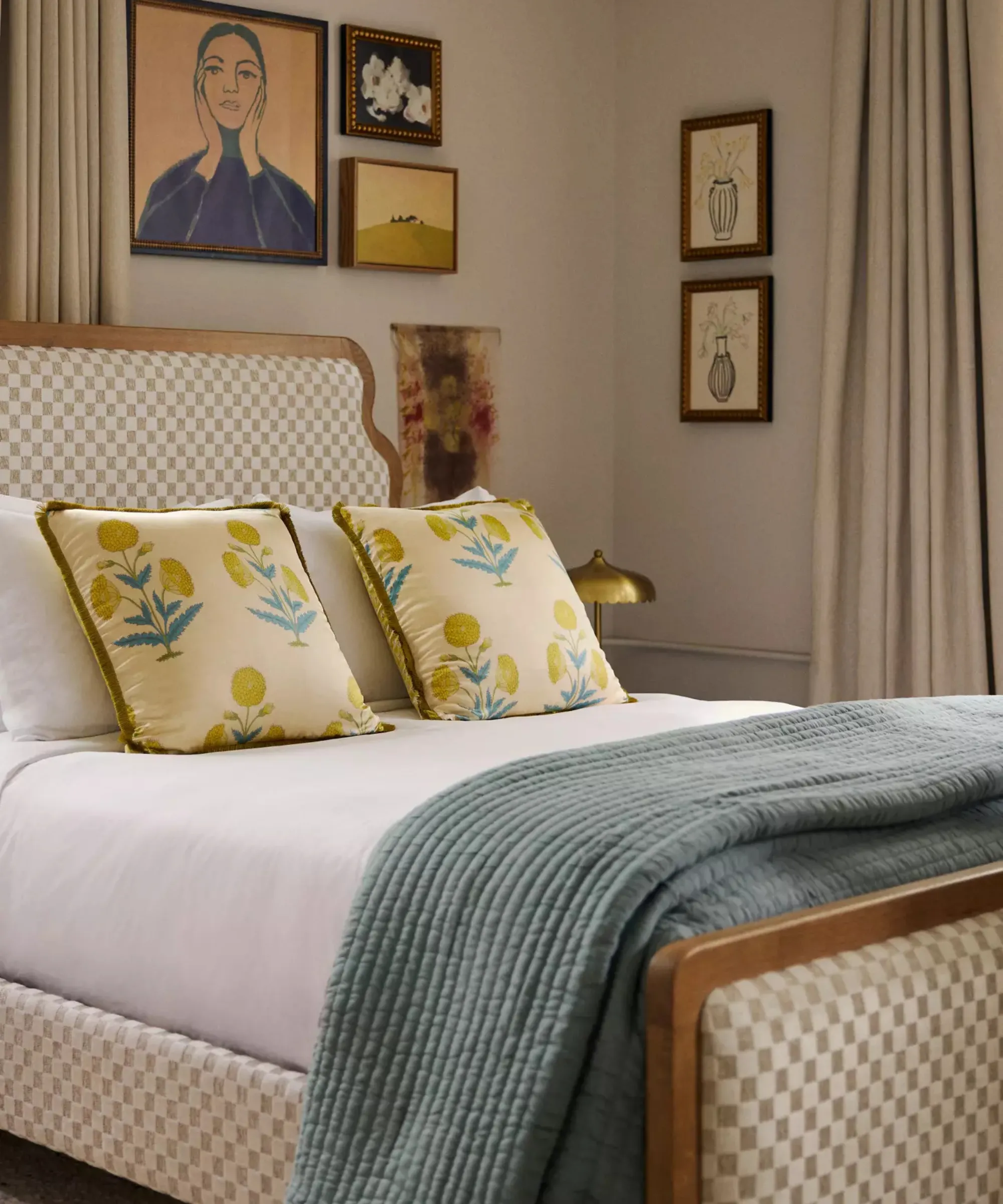 sypialnia z ramą łóżka w kratkę, białą pościelą, dwiema żółtymi poduszkami w kwiaty, turkusowy koc w nogach łóżka i grafika na ścianie za łóżkiem' loading='lazy' title=