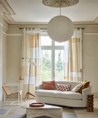 Beroligende, neutral moderne stue med abstrakte firkantede gardiner, lyse trægulve, afrundet papirlanterneskærm, buet creme sofa, gulvlampe, læder loungestol, marmor sofabord på tæppe