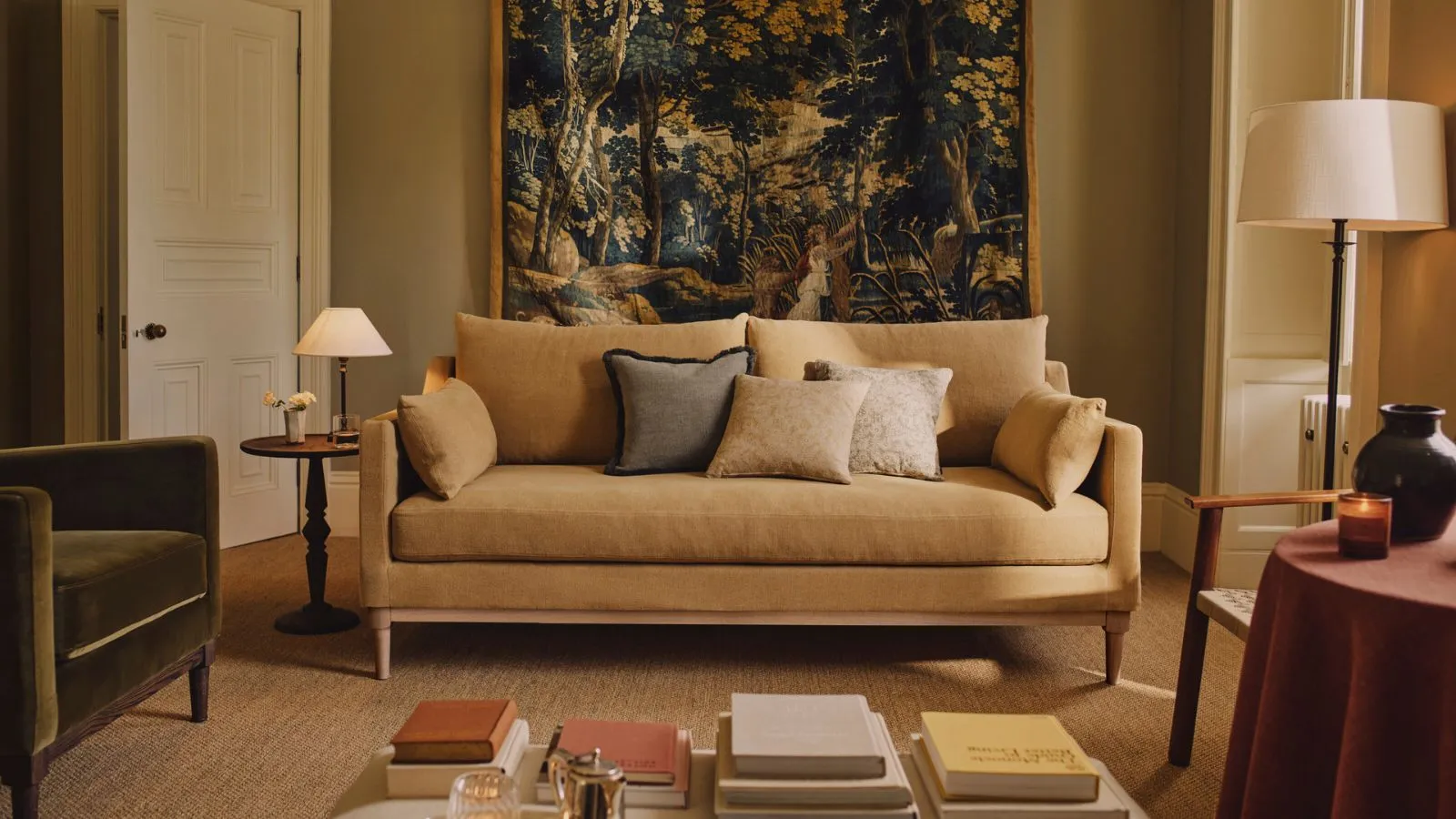 żółty salon z maślanożółtą kanapą i dużym gobelinem zawieszonym z tyłu stylizowanym na zielony aksamitny fotel i stoliki z lampkami' loading='lazy' title=