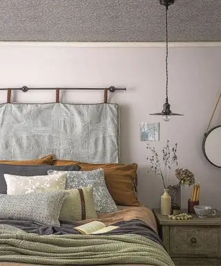 Nærbillede af en seng klædt med farvede tæpper og puder, natbord med en vase med græs.