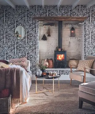 Hyggelig stue eller lunt med tændt brændeovn i hvidmalet alkove, lænestole og sofa med hynder og stofindtræk. Naturlige, efterårsfarver og toner.