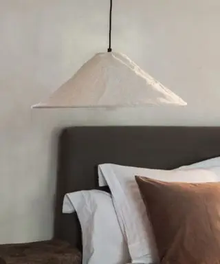 En brun sengeramme med lagdelte hvide og brune puder i baggrunden af ​​en lavthængende, lys beige pendel