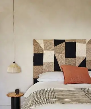 Un cabecero de patchwork multicolor con una pequeña mesita de noche redonda y una lámpara colgante baja.