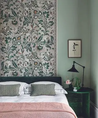 Un dormitorio verde con una cabecera característica, una mesita de noche pequeña con una pequeña lámpara negra y un cuadro pequeño colgado sobre la mesita de noche.