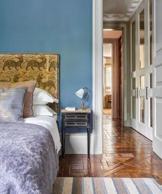 Chambre décorée en bleu avec parquet en bois, lit double avec literie grise et blanche et vue par la porte sur le palier.