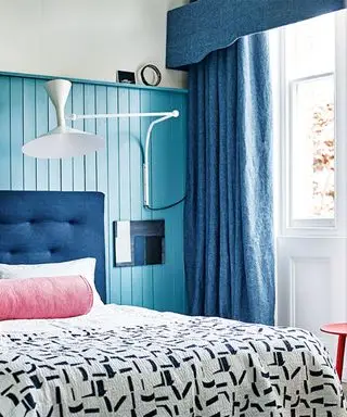 Pomysły na pomalowanie sypialni z pomalowaną na niebiesko boazerią, niebieskimi zasłonami i szpilkową poduszką na łóżku