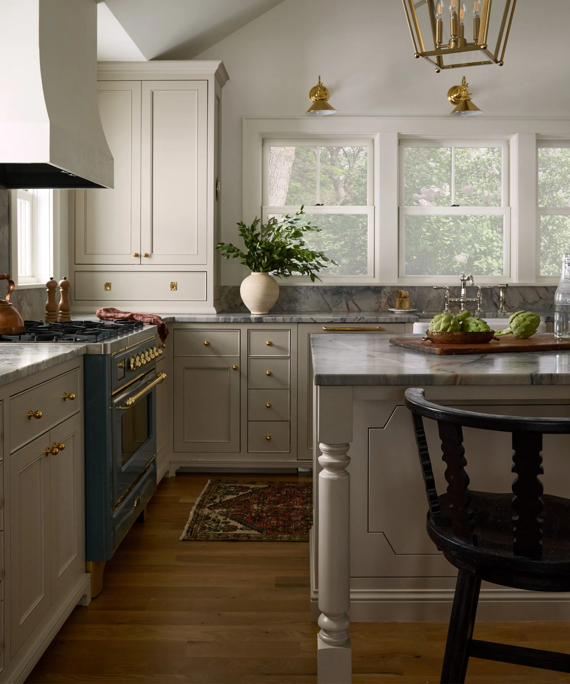 Cocina neutra con grandes ventanales que dan a la vista del lago, una gran campana extractora de yeso y encimeras de mármol azul.' loading='lazy' title=