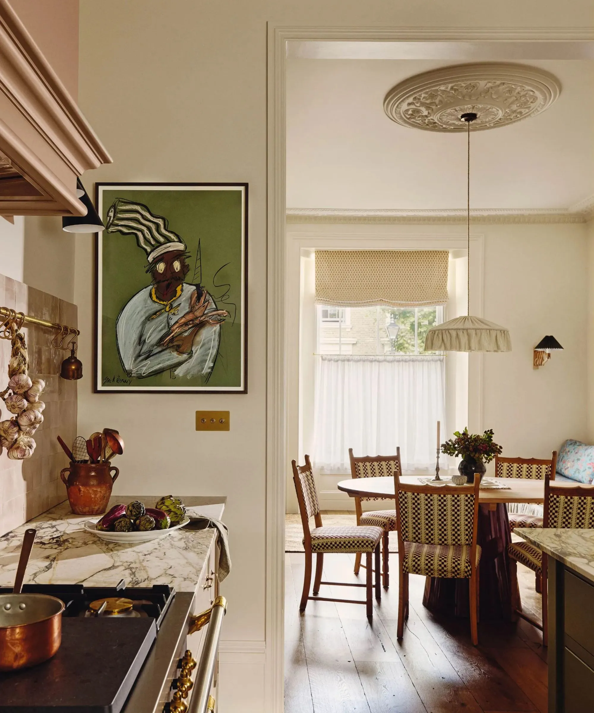 Un rincón de una cocina tradicional con encimeras de mármol, arte abstracto en la pared y una vista al comedor contiguo con una mesa redonda de madera y una gran lámpara colgante de tela encima' loading='lazy' title=
