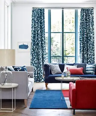 salón con paredes blancas, cortinas estampadas en azul oscuro y muebles azules y rojos