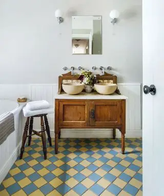 Meuble traditionnel en bois avec deux lavabos ronds dans une salle de bains avec carrelage victorien bleu et jaune.
