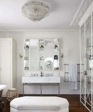 Um banheiro branco com lustre e pufe branco